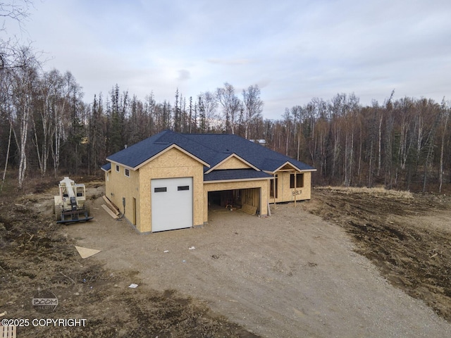 view of front of property with an attached garage, dirt driveway, stucco siding, and a wooded view