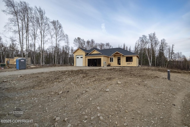 unfinished property featuring an attached garage and dirt driveway
