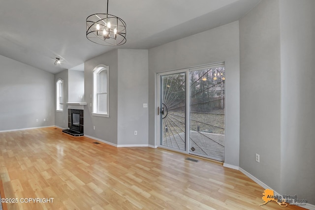 unfurnished living room featuring an inviting chandelier, vaulted ceiling, visible vents, light wood finished floors, and baseboards