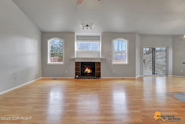 unfurnished living room with light wood finished floors, a tile fireplace, baseboards, and ceiling fan