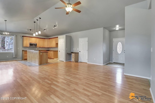 kitchen featuring open floor plan, stainless steel microwave, a center island with sink, and ceiling fan with notable chandelier