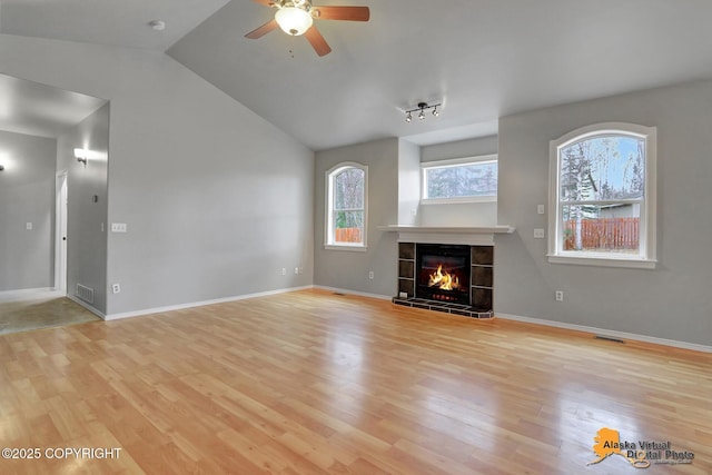 unfurnished living room with light wood-style flooring, visible vents, lofted ceiling, a tile fireplace, and ceiling fan