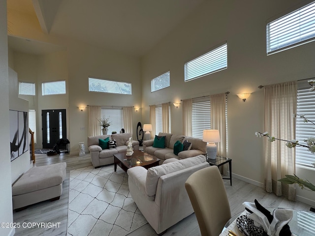 living room with baseboards, light wood-style floors, and a towering ceiling
