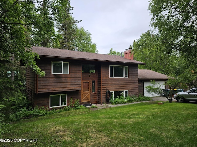 raised ranch featuring a chimney, a front lawn, roof with shingles, and a garage