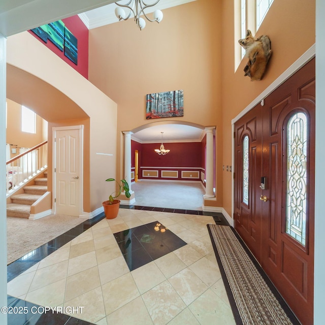 foyer featuring arched walkways, decorative columns, crown molding, and an inviting chandelier