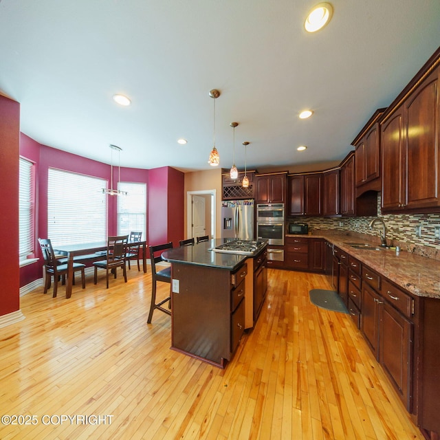 kitchen with a sink, light wood-type flooring, a kitchen island with sink, stainless steel appliances, and backsplash