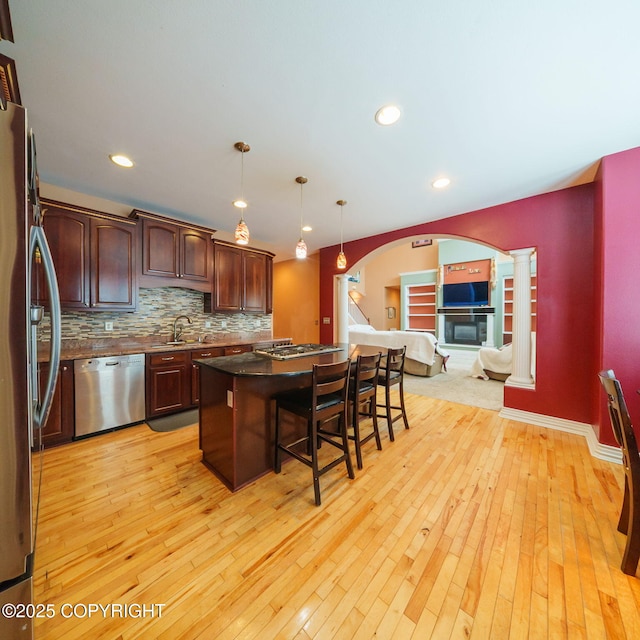 kitchen featuring arched walkways, appliances with stainless steel finishes, decorative columns, a kitchen island, and a breakfast bar area