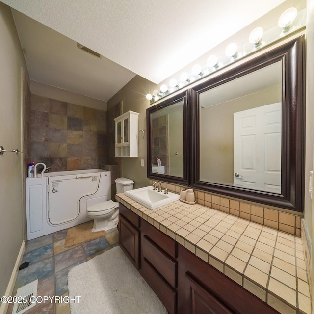 full bathroom featuring a bath, stone finish floor, vanity, a textured ceiling, and toilet