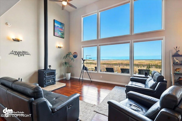 47366 Winridge Ave, Kenai, AK 99611 - living area featuring a wood stove, ceiling fan, hardwood / wood-style flooring, baseboards, and a high ceiling
