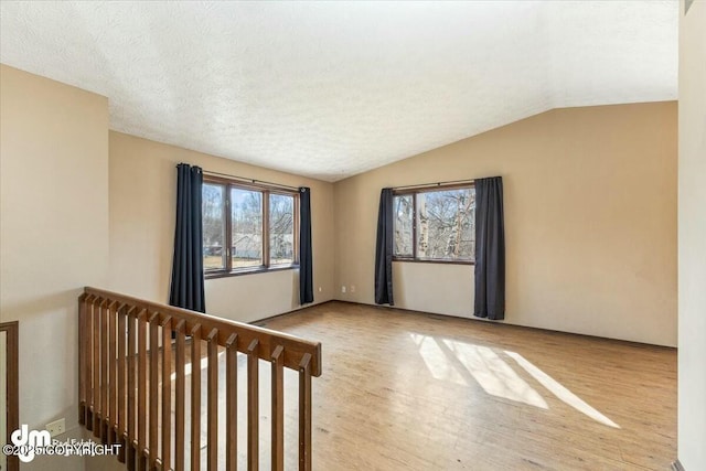 empty room featuring lofted ceiling, wood finished floors, a wealth of natural light, and a textured ceiling