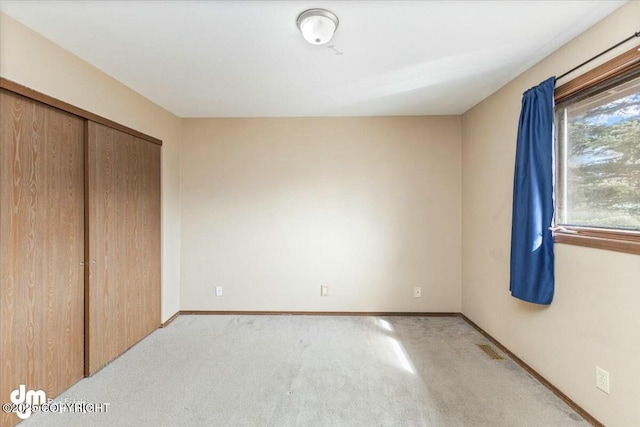 unfurnished bedroom featuring baseboards, a closet, and light colored carpet