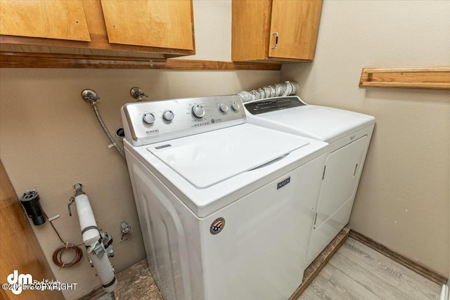 laundry room featuring washing machine and dryer, cabinet space, and light wood-type flooring