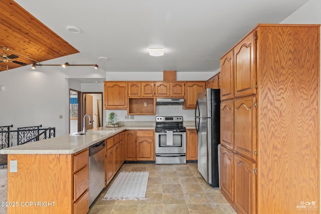 kitchen with a sink, light countertops, a peninsula, under cabinet range hood, and stainless steel appliances