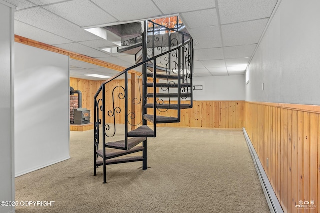 staircase with wood walls, a wood stove, a drop ceiling, and carpet floors