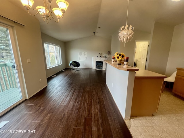 interior space with light countertops, vaulted ceiling, a fireplace, wood finished floors, and a notable chandelier