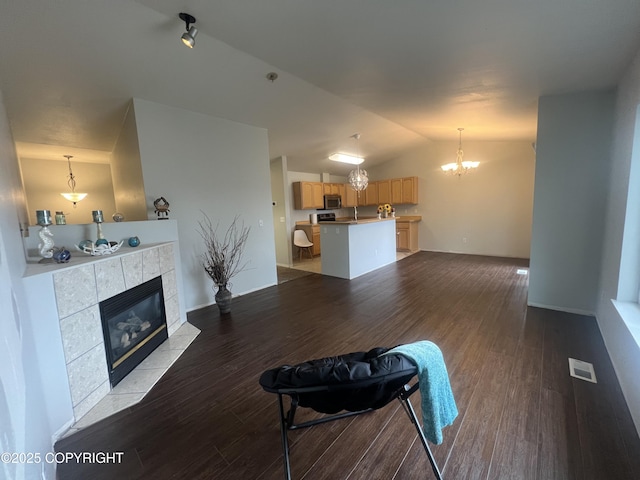 unfurnished living room with an inviting chandelier, dark wood-style flooring, a tiled fireplace, visible vents, and vaulted ceiling
