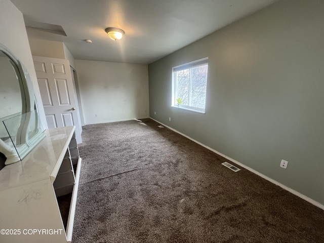 unfurnished dining area with visible vents, dark carpet, and baseboards