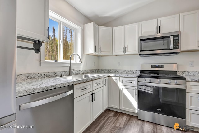 kitchen with appliances with stainless steel finishes, a sink, vaulted ceiling, white cabinetry, and wood finished floors