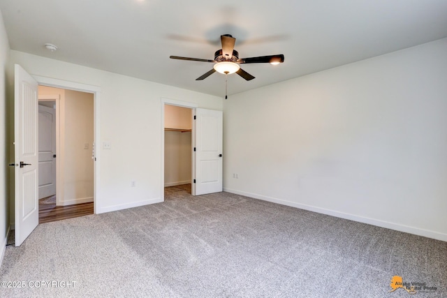 unfurnished bedroom with carpet floors, baseboards, a spacious closet, a ceiling fan, and a closet