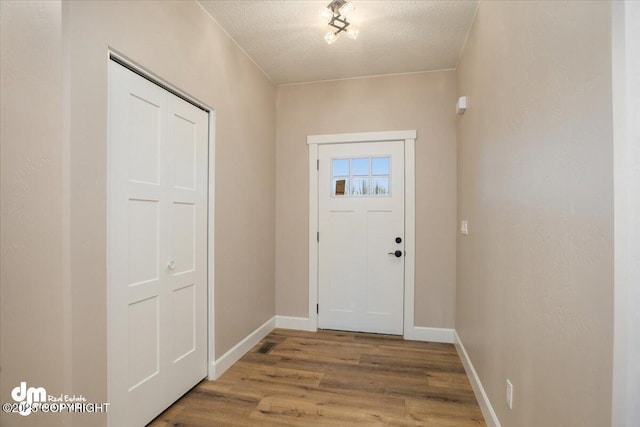 entryway with a textured ceiling, wood finished floors, and baseboards
