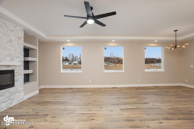 unfurnished living room with a fireplace, a raised ceiling, light wood finished floors, and ceiling fan with notable chandelier
