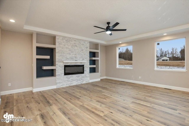 unfurnished living room featuring wood finished floors, a raised ceiling, ceiling fan, and baseboards