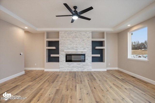 unfurnished living room featuring ceiling fan, hardwood / wood-style flooring, built in features, and a stone fireplace