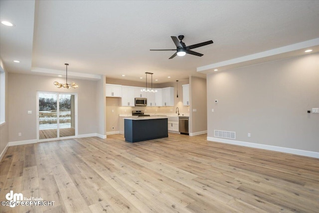 kitchen with light wood-type flooring, stainless steel appliances, ceiling fan with notable chandelier, and open floor plan