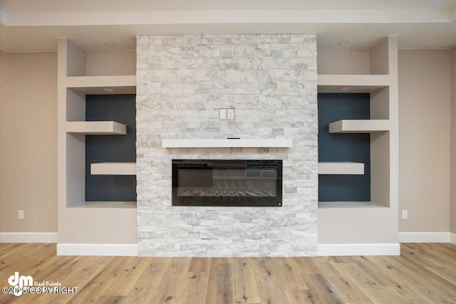 room details featuring baseboards, wood finished floors, built in features, and a stone fireplace