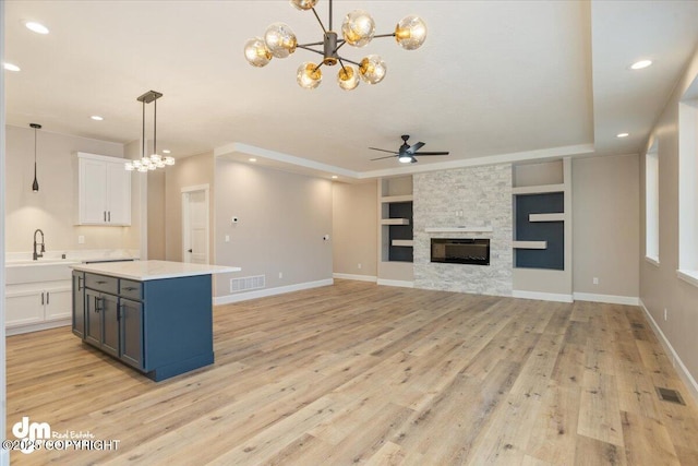 kitchen with a sink, visible vents, light countertops, built in features, and ceiling fan with notable chandelier