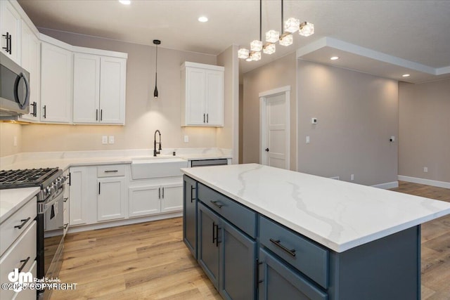 kitchen with light wood-style flooring, stainless steel microwave, gas stove, white cabinetry, and a sink