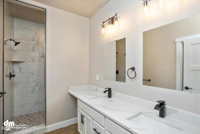 full bath featuring baseboards, a tile shower, double vanity, and a sink