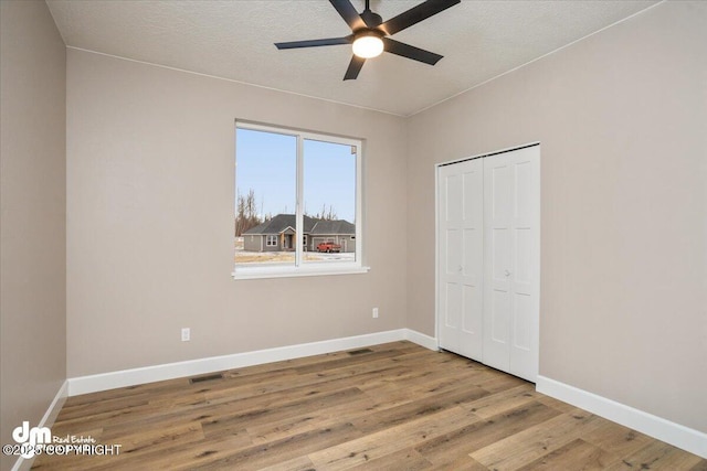 unfurnished bedroom with visible vents, a closet, baseboards, wood finished floors, and a ceiling fan
