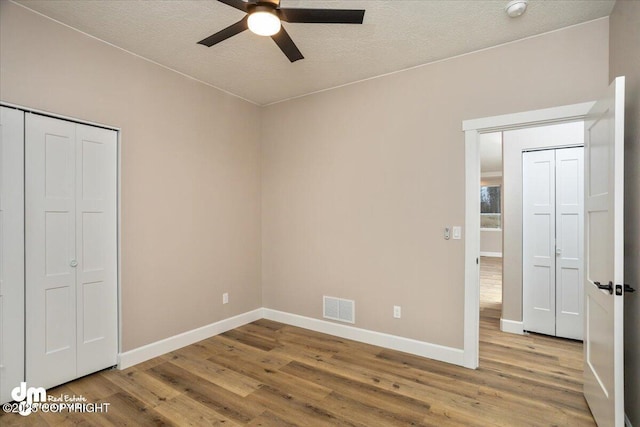 unfurnished bedroom with wood finished floors, visible vents, a textured ceiling, and baseboards