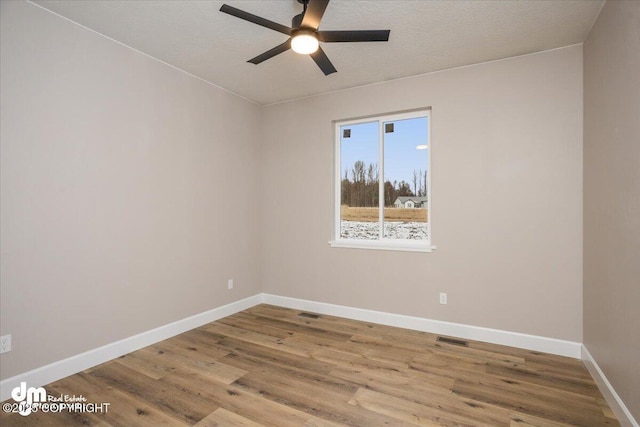 empty room with baseboards, visible vents, wood finished floors, and a ceiling fan