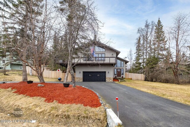 view of front of house featuring driveway, a garage, fence, a balcony, and stone siding