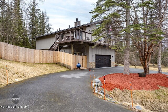 view of front facade featuring fence, a deck, a chimney, an attached garage, and driveway