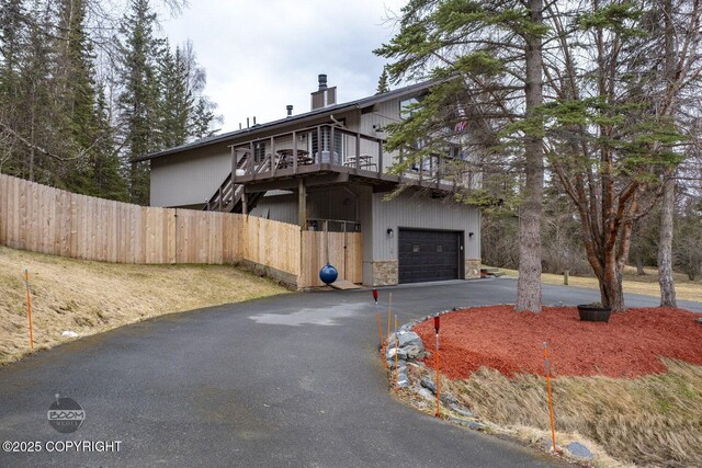 view of front of property with a chimney, a deck, a garage, fence, and aphalt driveway