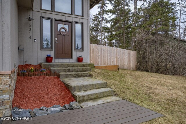 view of exterior entry with fence and a yard