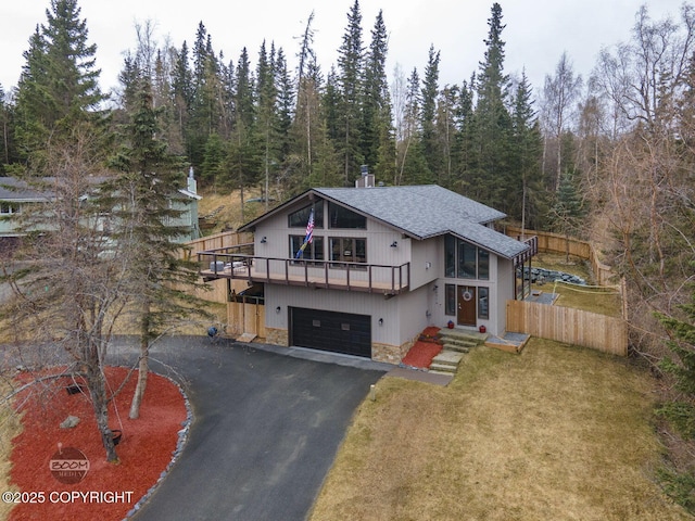 view of front of home with a garage, stone siding, roof with shingles, a view of trees, and driveway