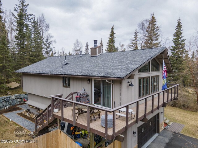 rear view of house featuring aphalt driveway, a deck, roof with shingles, a chimney, and an attached garage