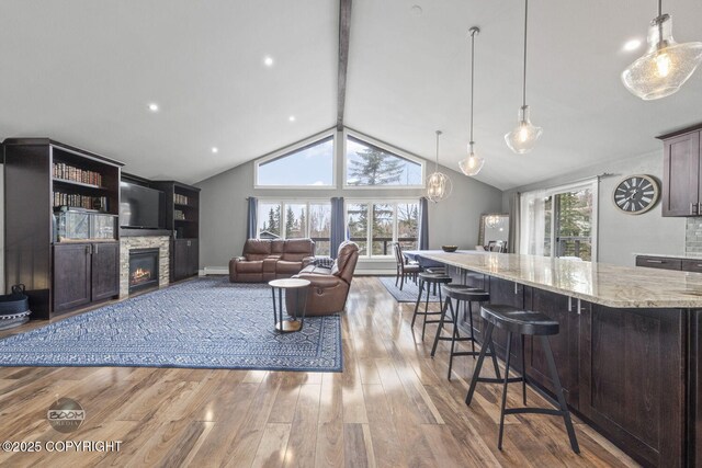 living room with a stone fireplace, lofted ceiling with beams, baseboards, and wood finished floors