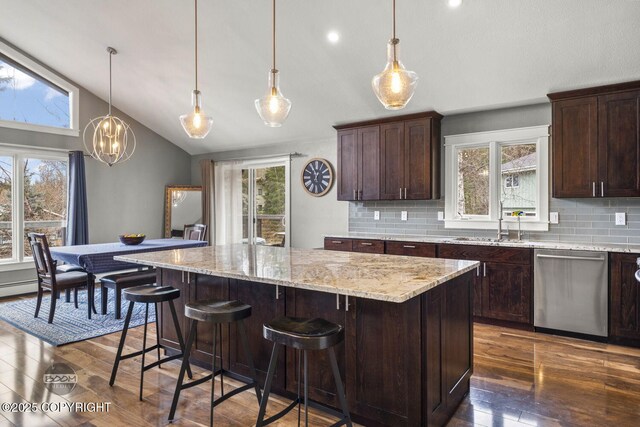 kitchen featuring stainless steel dishwasher, dark brown cabinetry, a kitchen island, tasteful backsplash, and dark wood finished floors