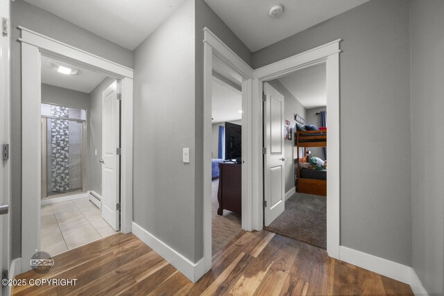 hallway with baseboards, light wood-style flooring, and a baseboard heating unit