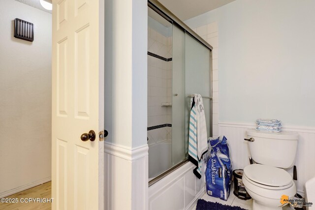 3210 Seawind Dr, Anchorage, AK 99516 - full bathroom with wainscoting, toilet, bath / shower combo with glass door, and wood finished floors