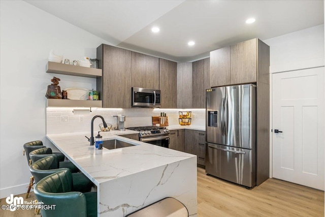 3460 S Shamrock St, Wasilla, AK 99623 - kitchen featuring appliances with stainless steel finishes, a sink, a peninsula, open shelves, and light stone counters