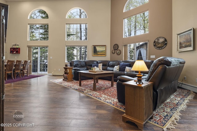 living area with a high ceiling, baseboard heating, wood-type flooring, and baseboards