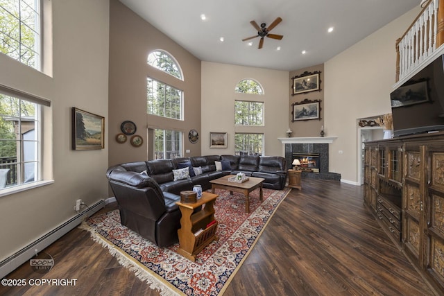 living area featuring a baseboard radiator, a towering ceiling, a ceiling fan, wood finished floors, and a fireplace