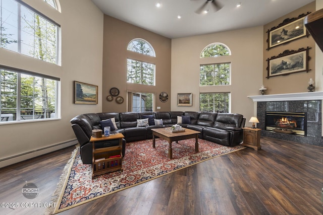 living room with hardwood / wood-style flooring, a towering ceiling, healthy amount of natural light, a tiled fireplace, and recessed lighting