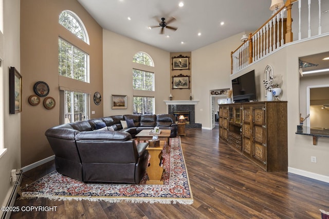 living room featuring a towering ceiling, a premium fireplace, hardwood / wood-style flooring, ceiling fan, and plenty of natural light